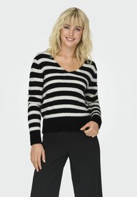 Schwarz-weißer gestreifter Pullover mit V-Ausschnitt, langen Ärmeln und weicher Textur; gerippter schwarzer Saum und Bündchen; kombiniert mit schwarzen Hosen.