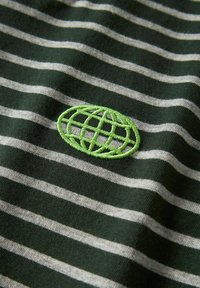 Donkergroene katoenen stof met horizontale witte strepen. Bevat een geborduurd groen wereldbollogo rechtsonder.