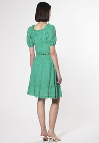 Vestido de algodón verde con mangas abullonadas, tejido texturizado, dobladillo con ondas y patrones recortados, combinado con sandalias blancas de tacón.