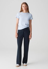 Helles blaues T-Shirt mit kurzen Ärmeln, kombiniert mit dunkeln marinefarbenen Hosen mit einem Kordelzugbund. Modell trägt weiße Sneaker mit einer hellen Sohle.