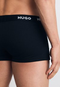 Boxers negros con una cinturilla suave que presenta el logo "HUGO" en blanco. Textura suave, diseño ajustado y longitud a mitad del muslo.