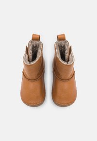 Botas de tobillo de cuero marrón con un suave forro de piel de color beige, punta redondeada y pestañas traseras para facilitar su puesta. Superficie exterior lisa con detalles de costura.