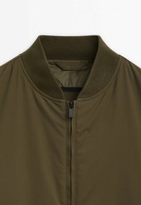 Blouson aviateur vert olive avec col côtelé, fermeture éclair avant et texture de tissu lisse, taille grande.