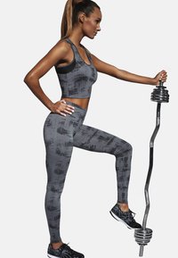 Szary sportowy crop top i legginsy z teksturowanym wzorem. Modelka podnosząca ciężarek, w czarnych sneakersach. Skupienie na odzieży sportowej.