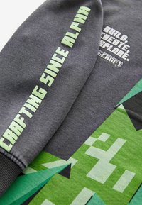 Sweatshirt gris avec un texte vert en gras indiquant "CRÉATION DEPUIS ALPHA." Présente un design graphique pixelisé vert avec des accents noirs.