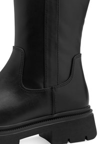 Bota alta de cuero negro con un acabado suave, costuras reforzadas y una suela de goma texturizada con un diseño de taco grueso.