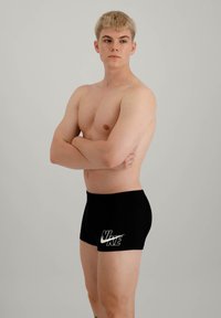 Shorts de bain Nike noirs avec un logo blanc à l'avant, fabriqués dans un matériau lisse, dotés d'un design ajusté et d'une longueur mi-cuisse.
