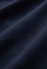 Glattes dunkel-navyblaues Gewebe mit dezenten Lichtreflexen und sanften Falten, die weiche Schatten erzeugen.