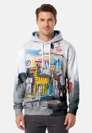 Man wearing a light gray hoodie with colorful abstract animal drawings, including yellow and black cats and dogs, on a white background.