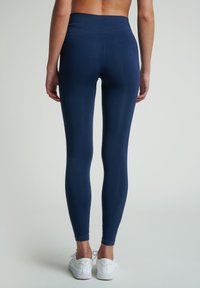 Marineblå leggings lavet af strækstof, med en høj talje og en glat tekstur, båret med hvide sneakers.
