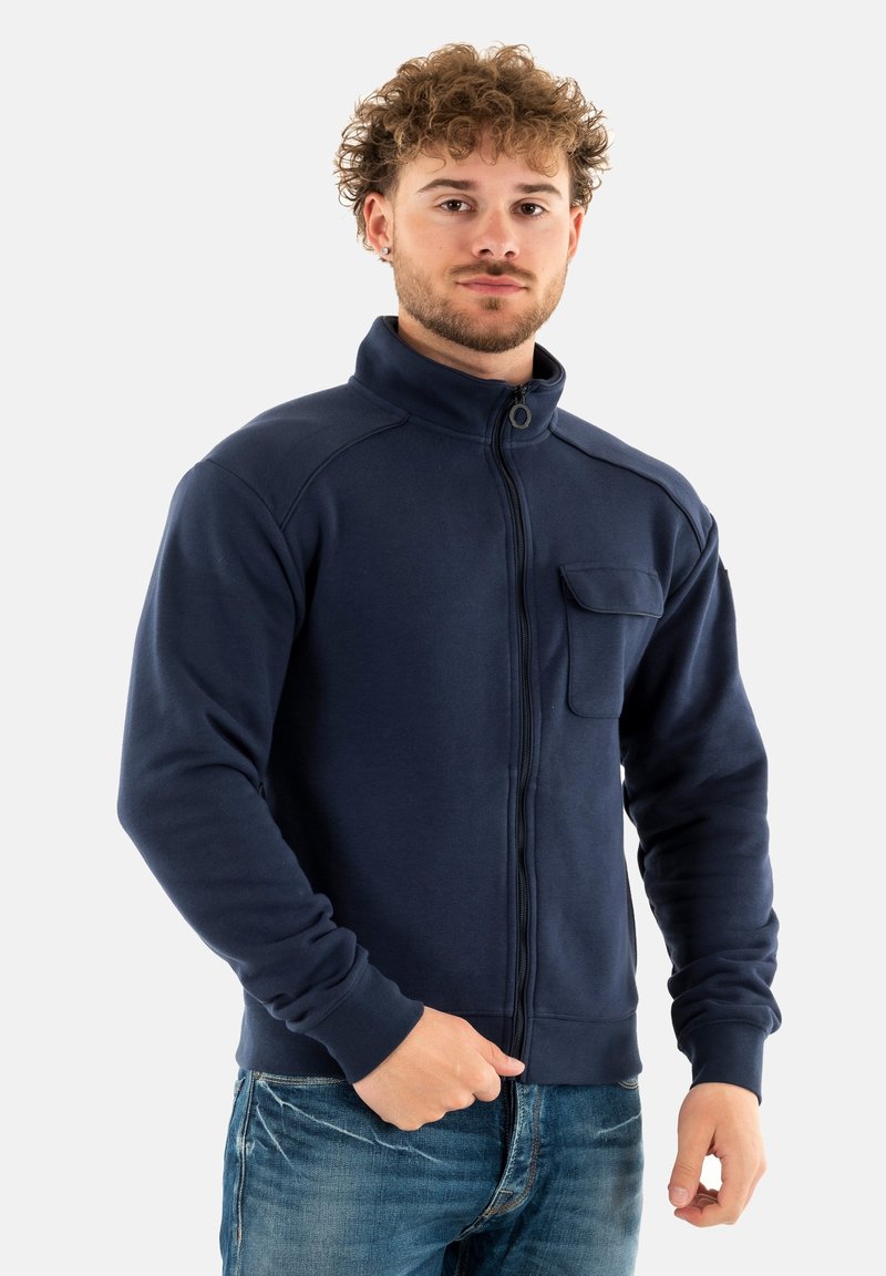 Felpa blu navy con zip, colletto alto, tasca anteriore, polsini e orlo a costine; realizzata in tessuto morbido con una superficie liscia.