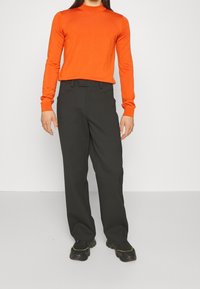 Pomarańczowy, długi, dzianinowy top z długim rękawem w połączeniu z czarnymi szerokimi spodniami. Top ma okrągły dekolt; spodnie mają klasyczny krój i szlufki na pasek.