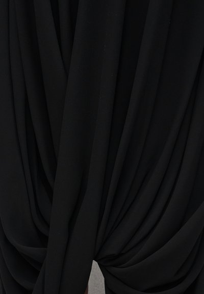 Μαύρο ύφασμα που πέφτει σε απαλές, ρέουσες πτυχές, δημιουργώντας στρωματοποιημένες, μαζεμένες υφές με ομαλή ματ επιφάνεια.