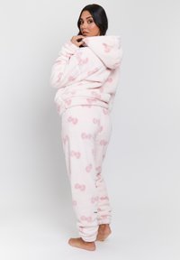 Fleece pyjamaset i ljusrosa med mönster av mörkare rosa rosetter. Har en huva och ribbade manschetter. Mjuk, texturerad tyg.
