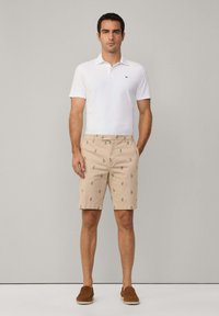 White polo shirt with short sleeves, beige shorts featuring green palm tree print, and brown slip-on shoes. Straight-fit silhouette.