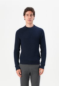 Dunkelblauer Strickpullover mit strukturiertem Muster, Rundhalsausschnitt und gerippten Manschetten und Saum. Kombiniert mit grauen Hosen.