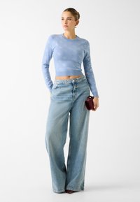 Maglione crop top azzurro chiaro con motivo circolare, abbinato a jeans a gamba larga azzurri chiari. Tieni una piccola borsa bordeaux.
