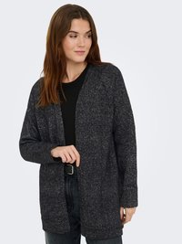 Woman wearing a dark gray knit cardigan over a black top, with dark jeans and a black belt, looking slightly to the side.