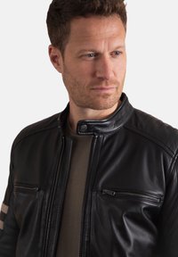 Black leather motorcycle jacket with quilted shoulder accents, zippered pockets, and a snap collar, worn over a gray top.