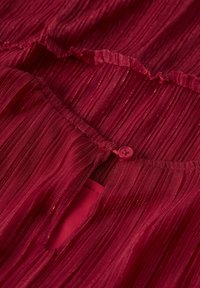 Nahaufnahme von tiefrotem plissiertem Stoff mit einem kleinen passenden Knopf, der eine Schlitzöffnung schließt.