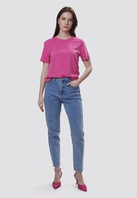 Lys pink bomulds t-shirt, lyseblå jeans med vertikale hvide striber og lyserøde højhælede sko. Enkel, tætsiddende design.