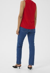 Top senza maniche rosso con design a occhio, abbinato a jeans blu a gamba dritta. Le scarpe nere con punta a mandorla completano l'outfit.