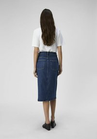 Jupe crayon en denim taille haute, de couleur bleue, avec deux poches arrière, et une longueur se terminant sous le genou. Associée à un t-shirt blanc et des escarpins noirs.