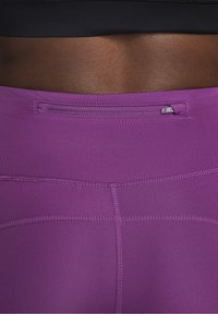 Leggings deportivos morados con una textura suave y elástica, que cuentan con un pequeño bolsillo en la parte trasera y detalles de costura en contraste.
