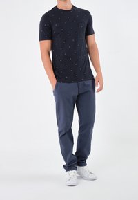 Marinblå t-shirt med kort ärm som har små vita prickar och en ficka. Tillsammans med marinblå byxor och vita sneakers, vilket skapar en avslappnad outfit.