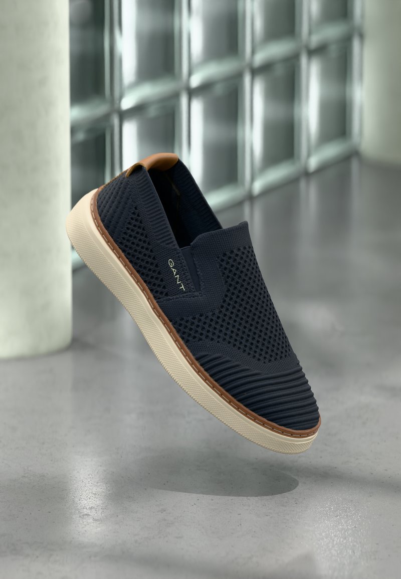 Chaussures à enfiler en mesh bleu marine foncé avec des accents texturés, semelle en caoutchouc crème, et détail beige au talon. Design léger.