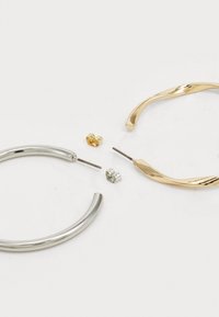 Zilveren en gouden creolen, met een gladde metalen afwerking, gebogen vormen en twee extra studoorbellen in zilver en goud.