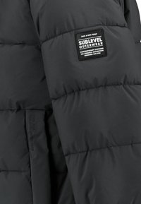 Black puffer jacket featuring a stitched design, smooth texture, and a prominent label. Designed for warmth and outerwear use.