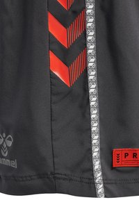 Zwarte sportshorts met rode chevronpatronen en grijze reflecterende details. Het label bevat het woord "PRO" in rood op een zwarte achtergrond.