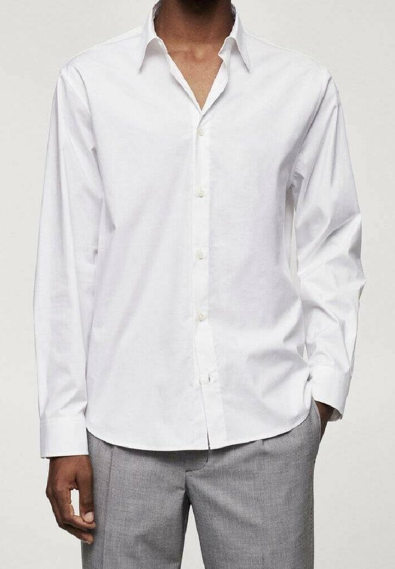 Chemise blanche en coton avec col classique, boutonnée à l'avant, manches longues et texture lisse, associée à un pantalon gris clair.