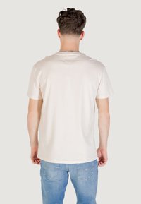 Beżowy bawełniany t-shirt z krótkimi rękawami i okrągłym dekoltem, pokazany od tyłu. W połączeniu z jasnoniebieskimi dżinsami.