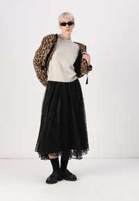 Leopardų rašto bomber tipo verslo striukė, pilkas svarkas su perlų akcentais, juoda nėrinių nosinaitė, juodos kojinės, masyvūs batai, elegantiški akiniai.