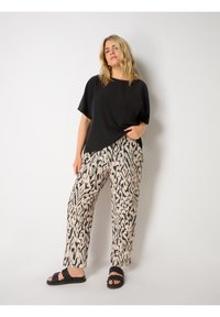 Svart kortärmad topp med ficka, matchad med beige och svarta mönstrade vida byxor. Modellen bär svarta flätade sandaler.