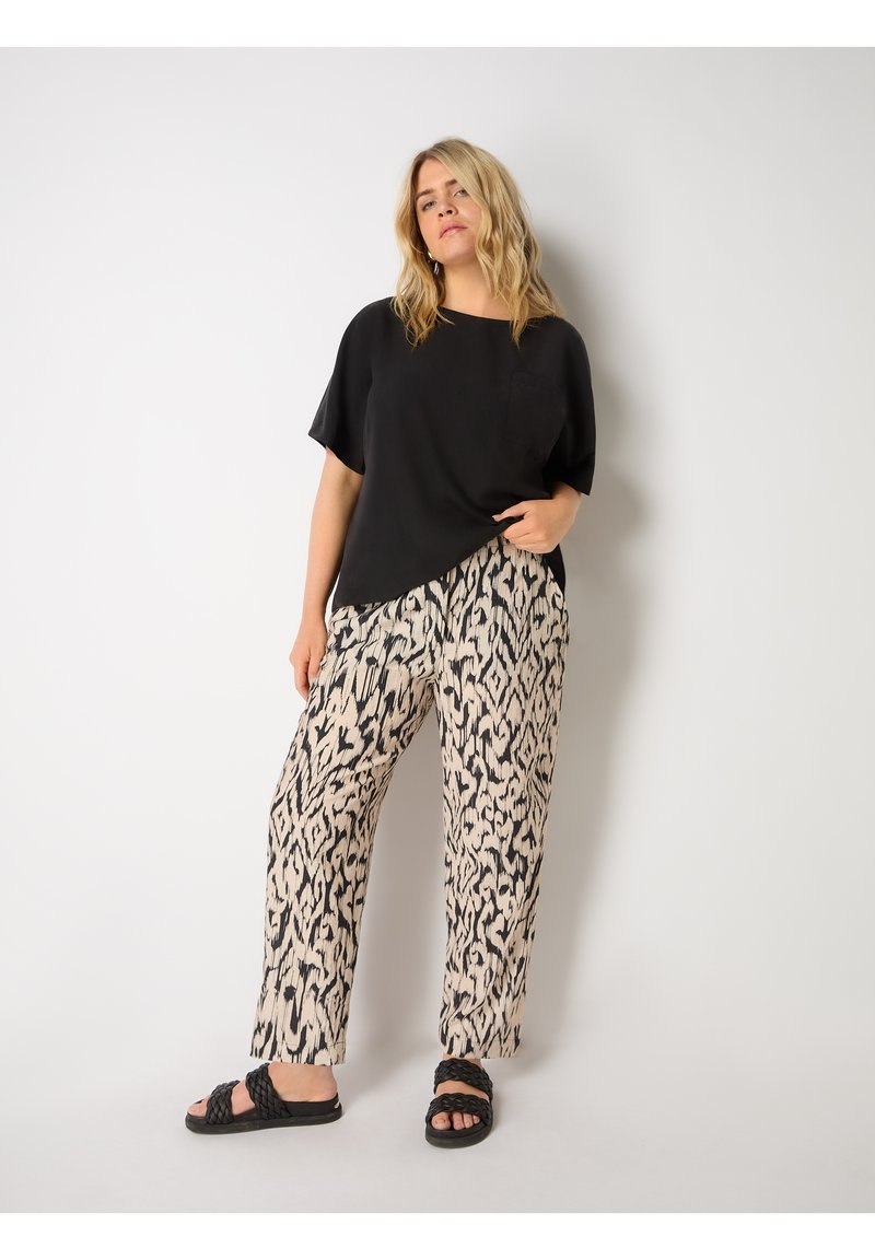 Svart kortärmad topp med ficka, matchad med beige och svarta mönstrade vida byxor. Modellen bär svarta flätade sandaler.