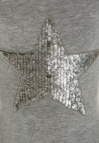 Šedé tričko s velkým designem hvězdy z stříbrných flitrů na přední straně, které dodává texturu a reflexní detaily látce.