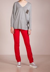 Graues Langarm-V-Neck-Oberteil mit texturierter Applikation, kombiniert mit roten Slim-Fit-Hosen und silbernen Sneakers. Weiches Material, entspannte Passform.