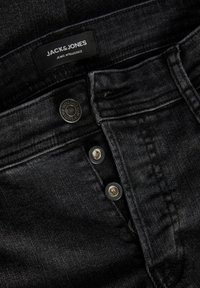 Svarta denimjeans med fem-knapps stängning och en sydd midja. Har en "JACK & JONES" etikett och en lätt blekning i tygets struktur.