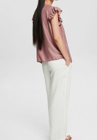 Lyserødlilla ærmeløs top med flæseærmer, parret med løse hvide bukser. Glat tekstur; enkel og afslappet design.