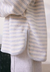 Pulover cu dungi în crem și albastru deschis, având tiv rotunjit, accente striate, material moale și design casual cu cusături laterale.