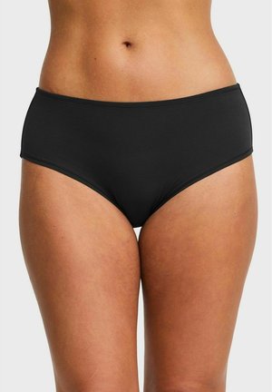 Vrouwelijke middenrug gekleed in effen zwarte, hoog uitgesneden ondergoed, met zicht op de buik en de bovenbenen tegen een witte achtergrond.