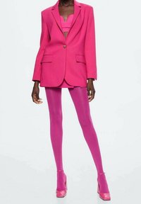 Heller rosa übergroßer Blazer mit zwei Fronttaschen, kombiniert mit passenden rosa Leggings und High Heels. Glatte Textur über die gesamte Fläche.