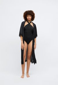 Melna satīna halātiņš ar mežģīņu apdari, valkāts virs melna viengabala peldkostīma. Šaura piegriezuma, ar halter stila kakla griezumu un atvērtu priekšpusi. Gluda tekstūra.