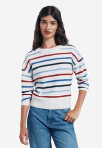 Gestreifter Pullover in Weiß, Rot, Blau und Schwarz mit Rundhalsausschnitt und drei Viertelärmeln, kombiniert mit blauen Jeans.