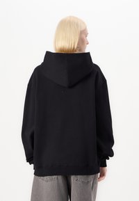 Black hooded sweatshirt with a relaxed fit, featuring a kangaroo pocket and ribbed cuffs. Smooth texture, minimal branding, and no embellishments.