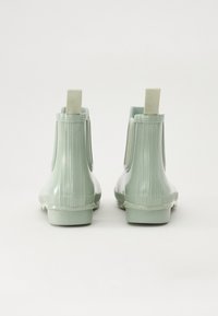 Bottes de cheville en caoutchouc vert avec texture nervurée, languettes à l'arrière et finition lisse. Semelles plates pour la stabilité et le confort.