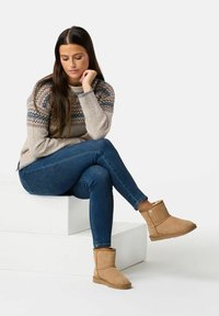 Hellbraune Wildleder-Ankle Boots mit einem weichen Innenfutter, kombiniert mit blauen Jeans und einem hellgrauen Pullover mit einem gemusterten Yoke-Design.